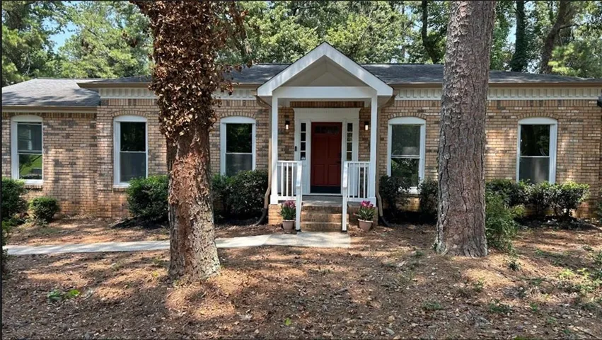 Brick facade home with a covered front porch, white columns, and a deep red entry door