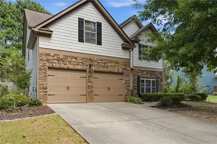 Exterior featuring a two-car garage, stone veneer siding, light-colored siding, and dark shutters
