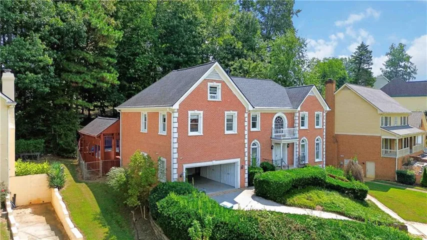 Red brick exterior with white trim, arched portico, upper balcony with balustrade, attached two-car garage, and established landscaping