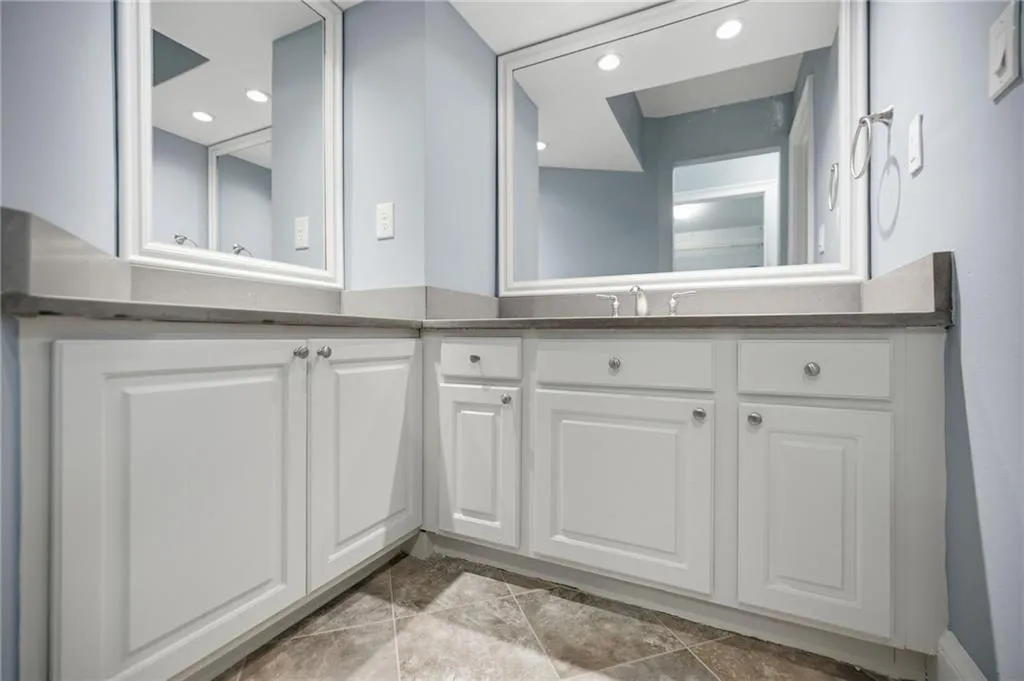 White cabinetry with panel detailing, dual framed mirrors, integrated sink, and tiled flooring