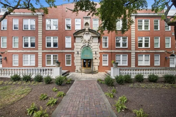 Brick facade building featuring a grand entrance with ornate architectural details, white window frames, and a classic balustrade