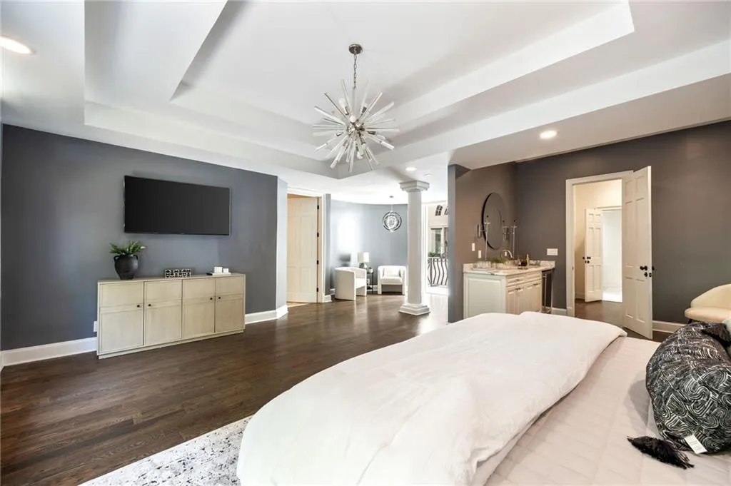 Bedroom with recessed lighting, a tray ceiling, dark wood finished floors, decorative columns, and a chandelier