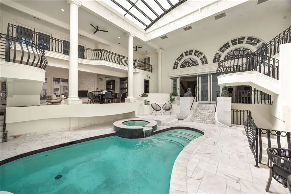 View of pool with a skylight, a pool with connected hot tub, ceiling fan, and decorative columns