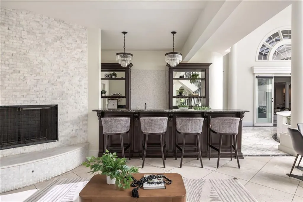 Bar area with a fireplace with raised hearth, pendant lighting, light tile patterned floors, a chandelier, and dark stone counters