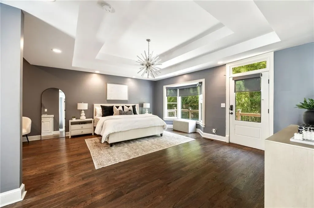 Bedroom featuring dark wood-style floors, arched walkways, a tray ceiling, access to exterior, and a chandelier