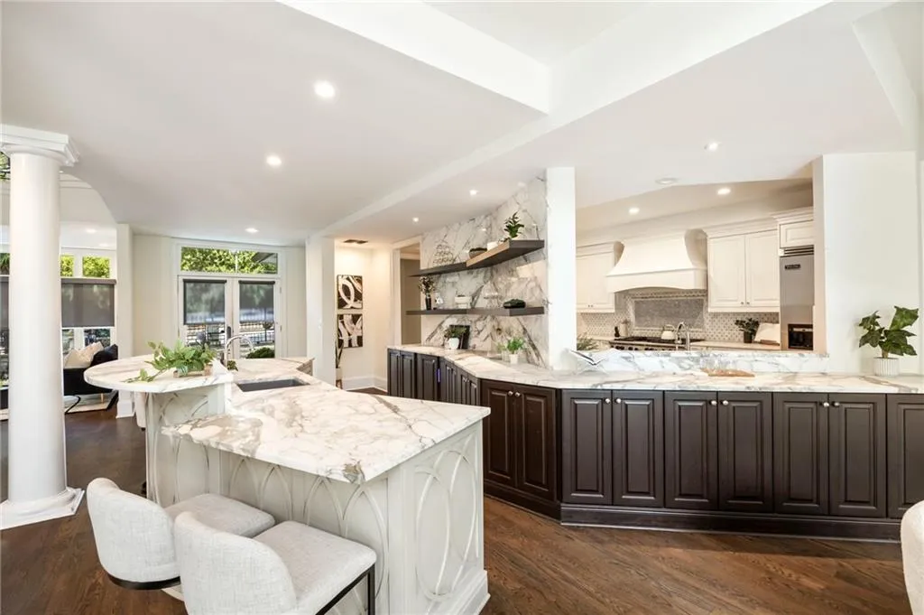 Bar with white cabinets, light stone counters, tasteful backsplash, open shelves, and ornate columns