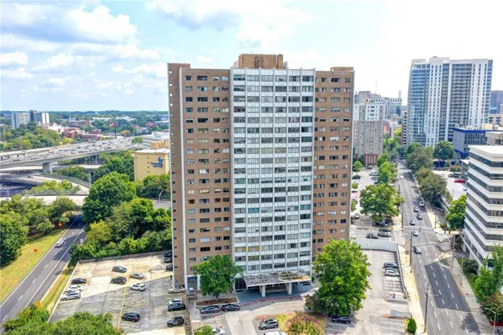 High-rise building featuring multiple levels of balconies, a prominent entrance canopy, and an expansive parking area