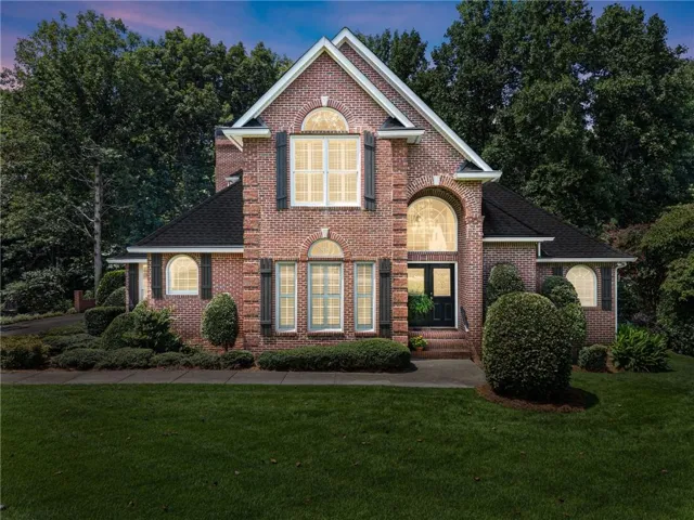 Elegant brick Colonial featuring a symmetrical facade with arched entryways, multi-pane windows with decorative pediments, and a prominent gabled roofline