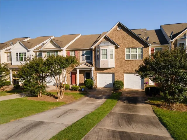 Brick and siding townhome featuring a pitched roof, bay window, white garage doors, and a concrete driveway
