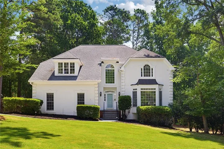 White stucco exterior featuring a grand arched window, a bay window with a dark metal awning, multiple dormer windows, and a light blue front door