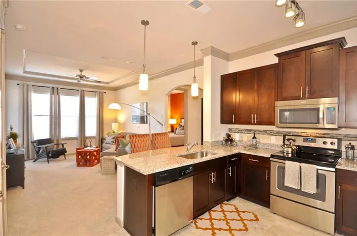Kitchen featuring kitchen peninsula, a tray ceiling, hanging light fixtures, appliances with stainless steel finishes, and ornamental molding