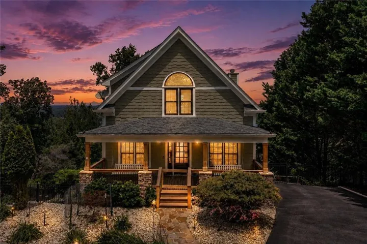 Gable roofline with an arched window, shake siding, covered front porch with wood columns and stone bases, stone steps, and a paved driveway