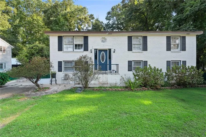 White brick exterior with dark shutters, front porch with metal railing, and a vibrant green lawn