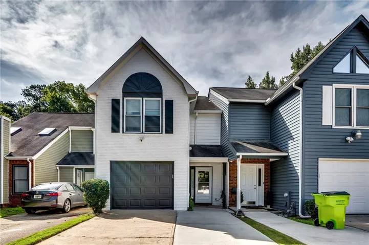 White brick facade with dark shutters, arched window accent, and an attached garage
