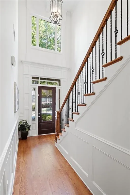 Two-story foyer featuring wood-finish flooring, wainscoting, and a prominent staircase with iron balusters