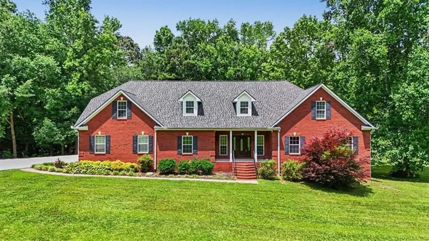 Traditional brick residence featuring a dark shingle roof, multiple dormer windows, and black louvered shutters