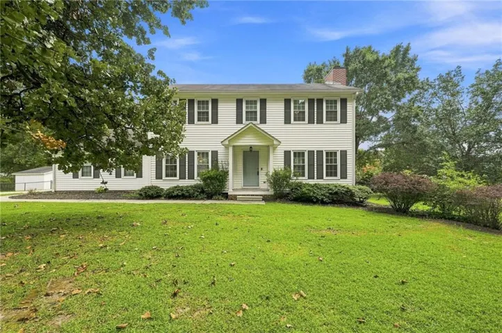 Colonial-style exterior featuring white siding, dark window shutters, a covered entry, and mature landscaping