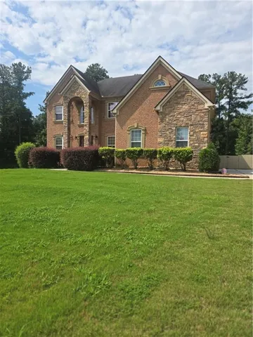 Two-story brick facade with stone accents, arched entryway, gabled rooflines, and a spacious front lawn