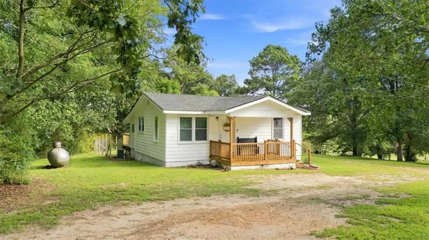 White exterior siding with a covered porch, wood railing, and a side deck
