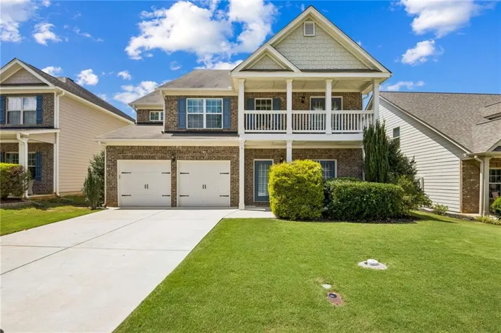 Brick and siding exterior featuring a two-car garage, upper-level balcony, and a manicured lawn
