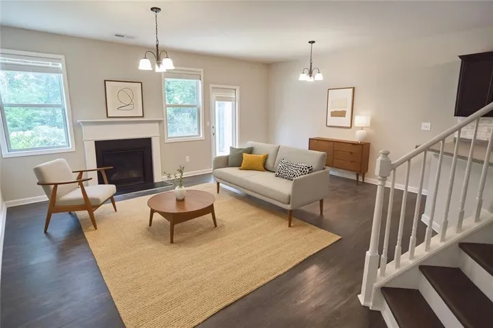 Living space featuring dark wood-finish flooring, a fireplace with a white mantel, and multiple windows