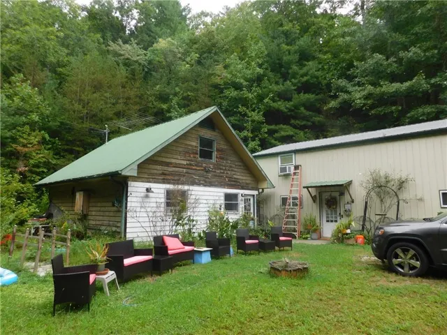 Wood siding with a green metal roof, a second structure with light-colored siding and a matching green metal awning over the entry, and a natural wooded backdrop