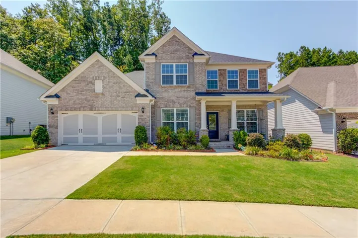Brick facade, covered front porch with columns, two-car garage, manicured lawn, and mature landscaping
