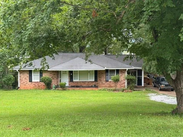 Brick ranch exterior featuring a covered front porch, dark-shingle roof, and a gravel driveway