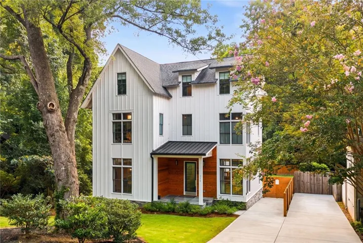 Modern farmhouse exterior with white vertical siding, black-framed windows, a dark metal roof over the entry, a wood-paneled porch, and a concrete driveway