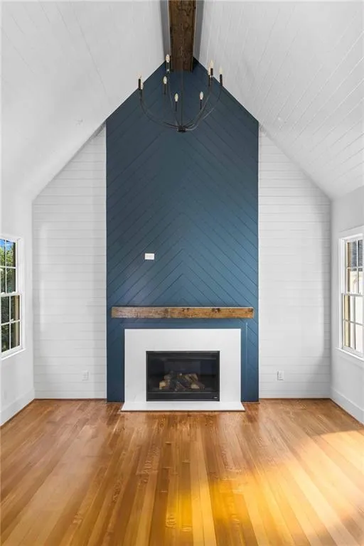 Unfurnished living room featuring healthy amount of natural light, a glass covered fireplace, wood-type flooring, and wood walls