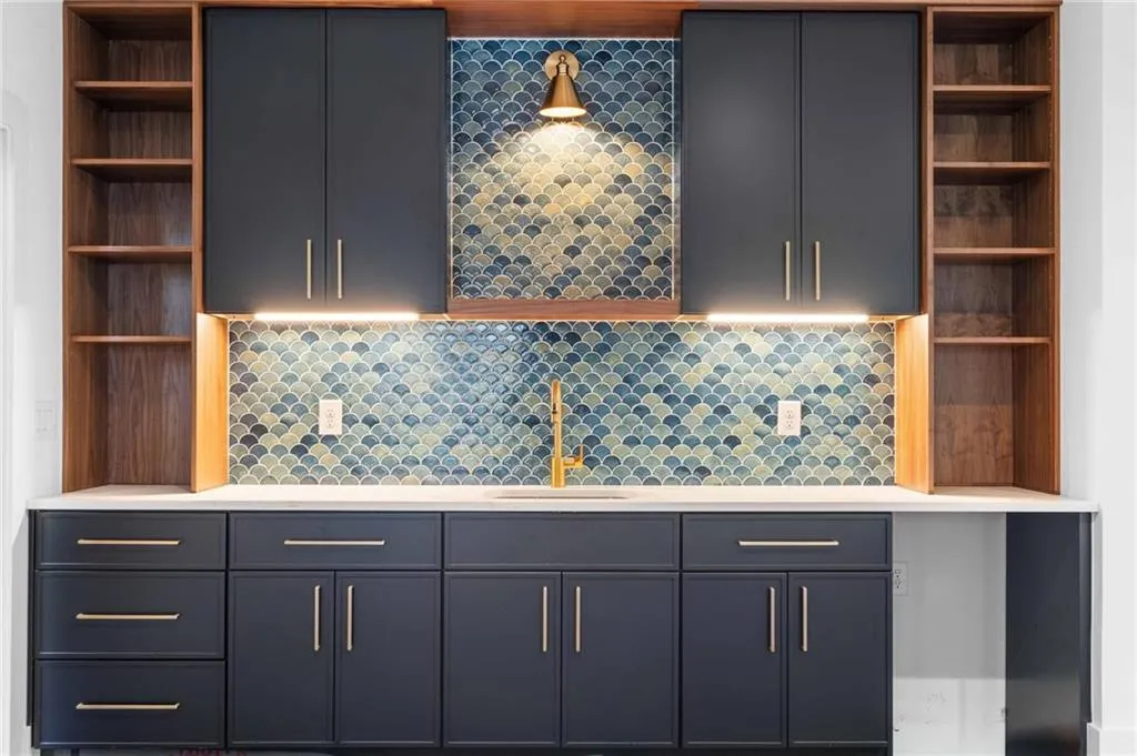 Kitchen with open shelves, dark cabinets, backsplash, and light stone countertops