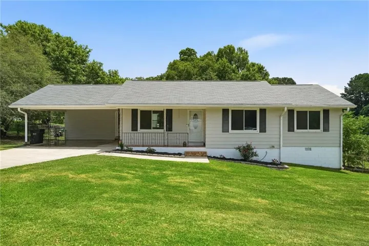 Single-story residence featuring light-colored siding, a covered carport, and a prominent front lawn
