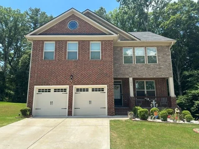 Two-story residence featuring a brick and stone facade, a two-car garage with carriage-style doors, and a covered front porch