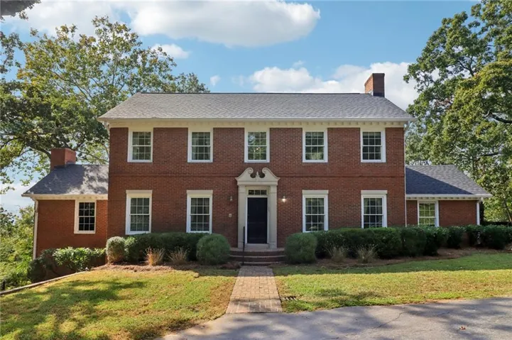 Colonial house with a chimney, brick siding, a front lawn, and a shingled roof