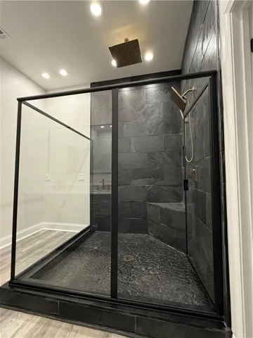 Glass-enclosed shower with dark stone-tiled walls, a built-in bench, and a unique pebble-style floor