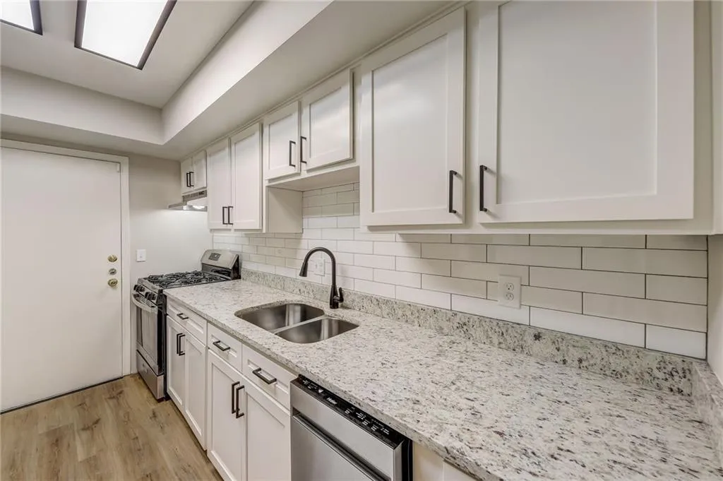 Kitchen with stainless steel appliances, white cabinetry, sink, and light wood-type flooring