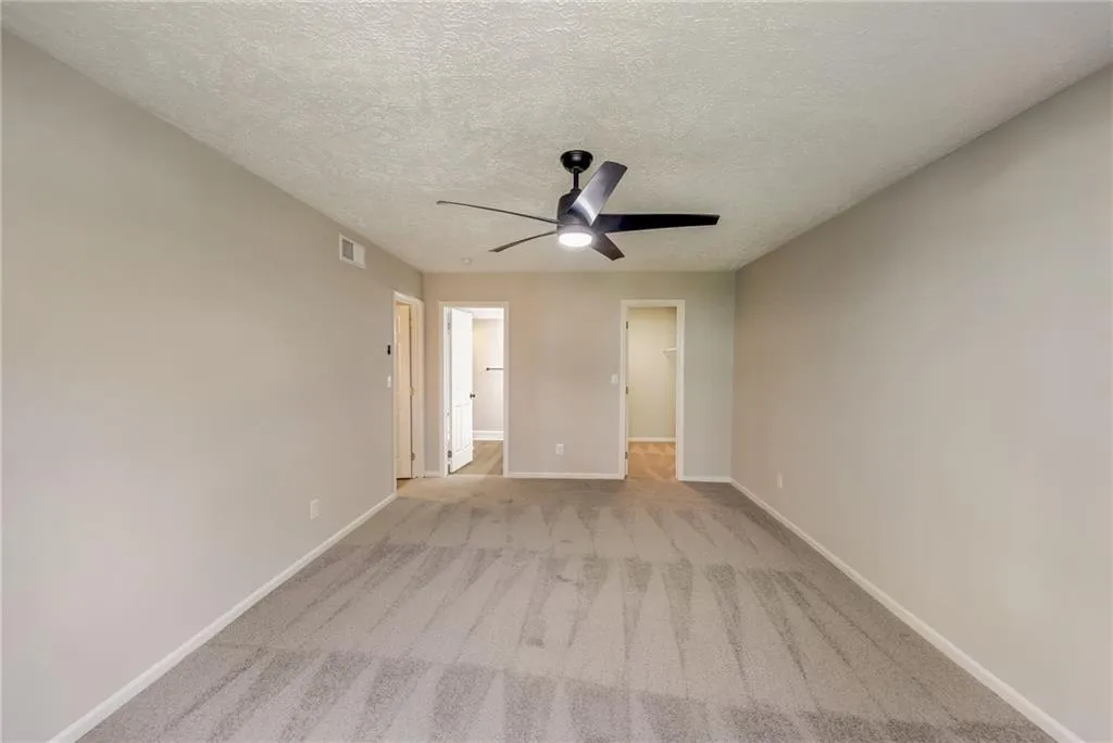 Carpeted empty room with ceiling fan and a textured ceiling