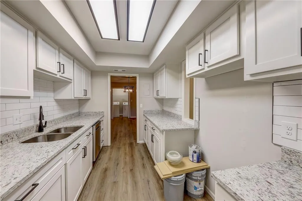 Kitchen with white cabinetry, backsplash, light hardwood / wood-style floors, light stone counters, and sink