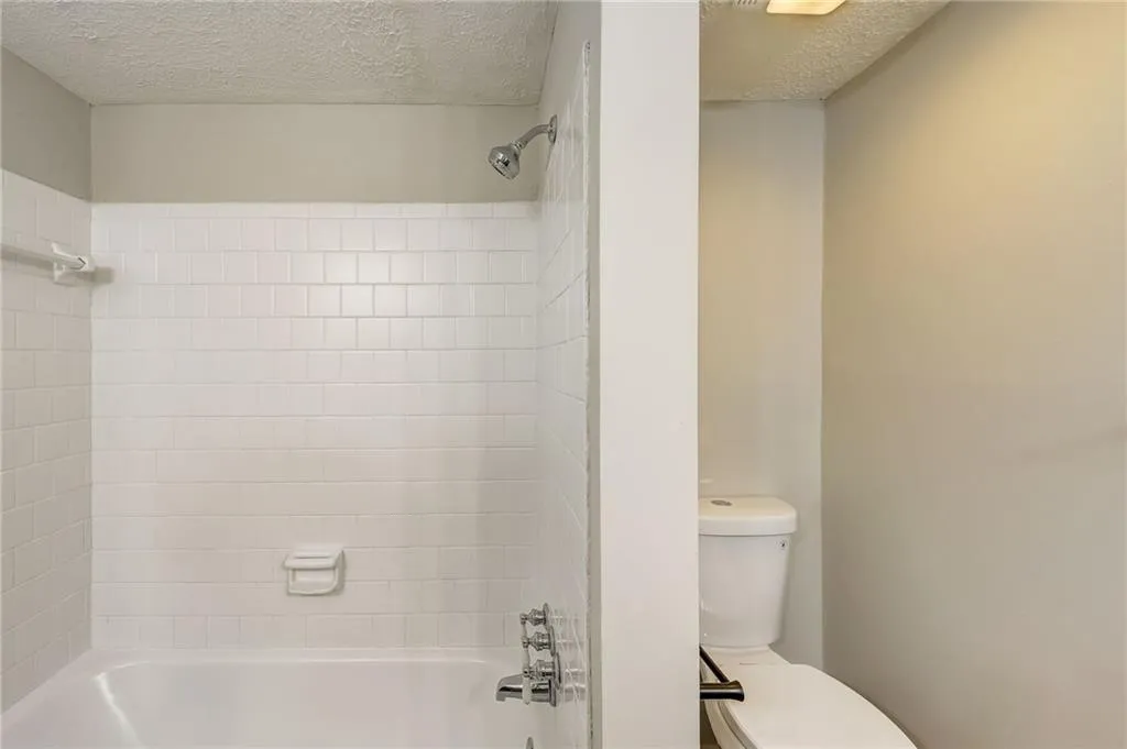 Bathroom featuring tiled shower / bath combo, a textured ceiling, and toilet