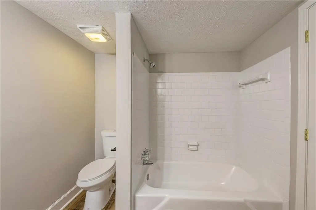 Bathroom with tiled shower / bath, wood-type flooring, toilet, and a textured ceiling