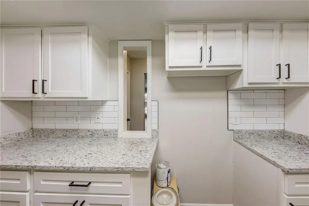 Kitchen featuring backsplash, light stone counters, and white cabinetry
