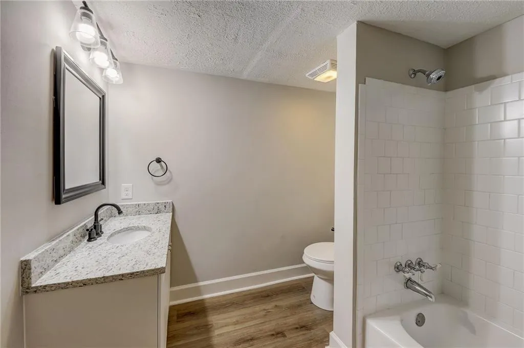 Full bathroom featuring tiled shower / bath, vanity, hardwood / wood-style floors, toilet, and a textured ceiling