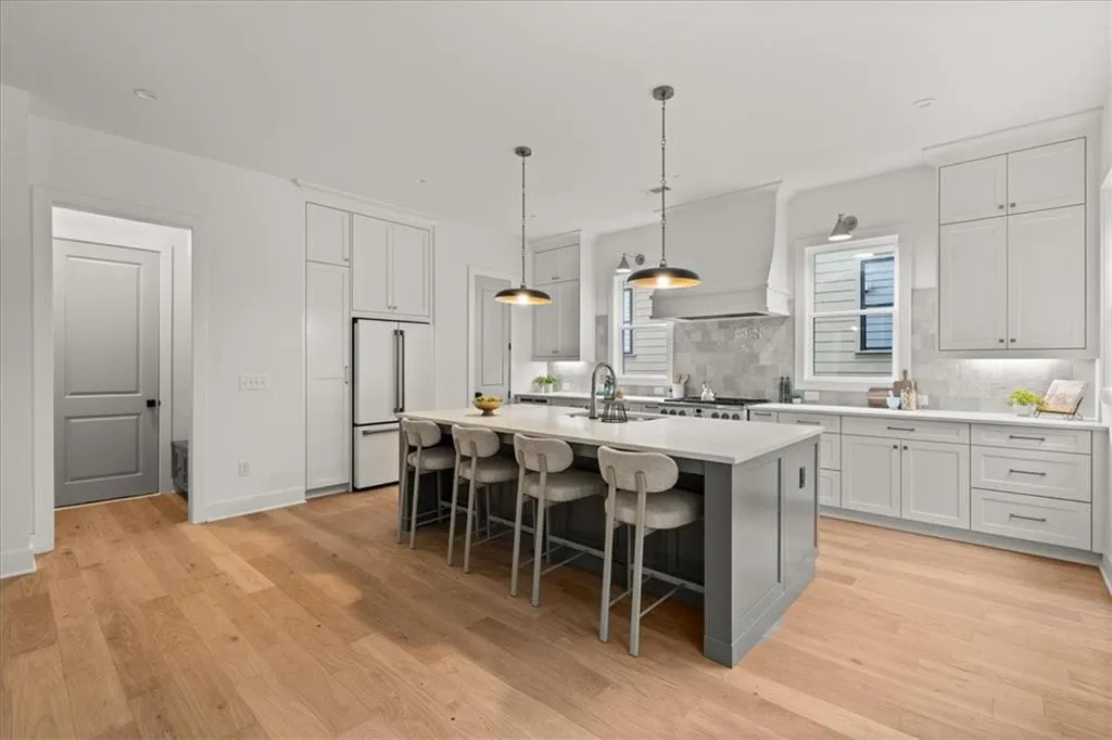 Kitchen featuring decorative backsplash, a kitchen island with sink, pendant lighting, a breakfast bar area, and light wood-style floors