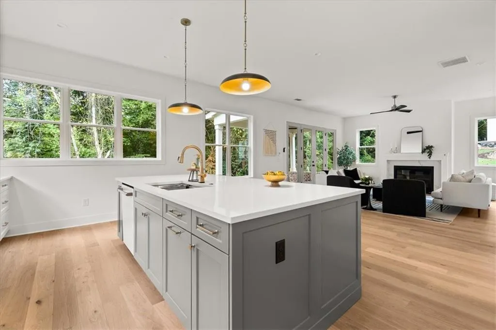 Kitchen featuring gray cabinets, decorative light fixtures, an island with sink, and light wood-style floors