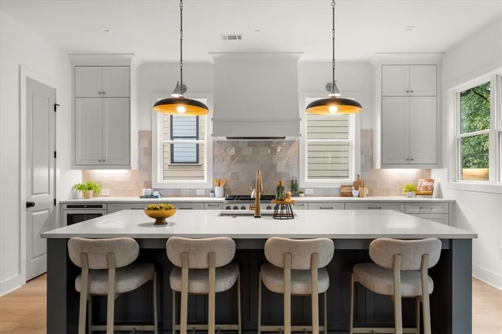 Kitchen featuring light wood-style floors, decorative backsplash, an island with sink, and hanging light fixtures