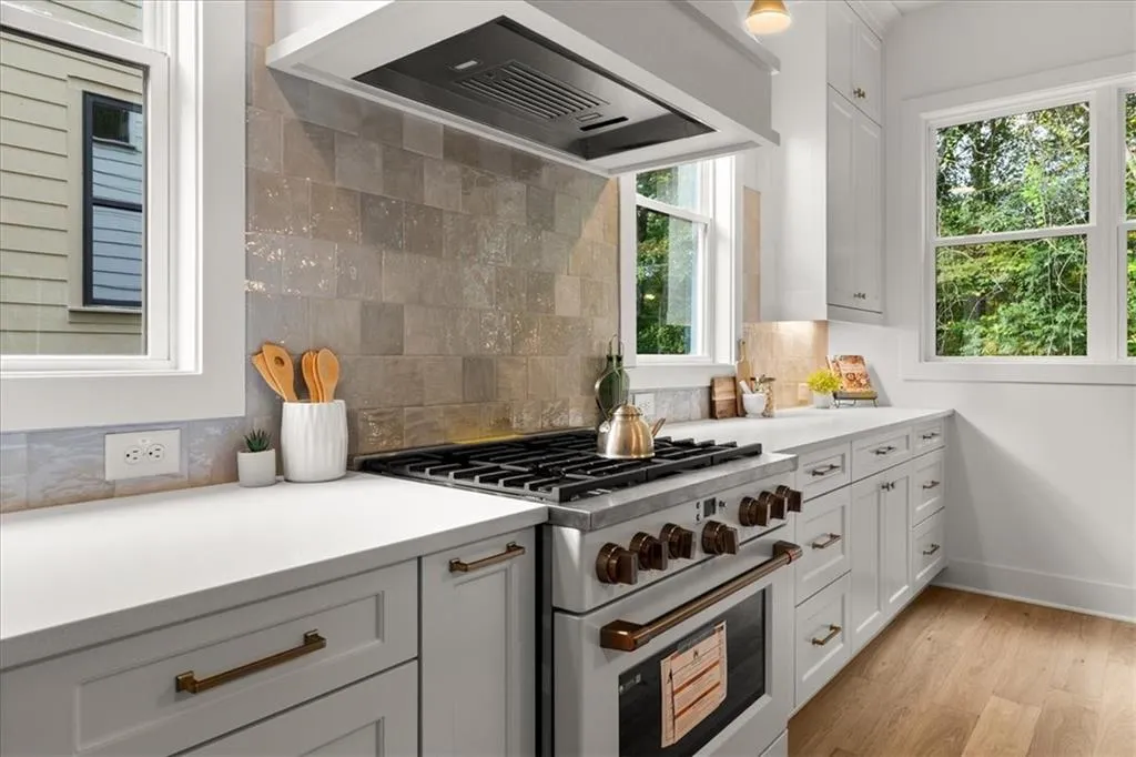 Kitchen with custom exhaust hood, high end range, decorative backsplash, white cabinets, and light wood-type flooring