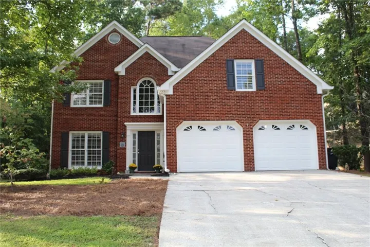 Brick exterior with white trim, featuring a two-car garage, an arched window, and a dark front door with sidelights