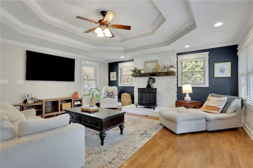 Living room with a raised ceiling, a wood stove, crown molding, and light wood-type flooring
