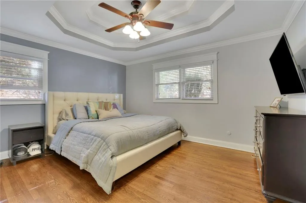 Bedroom featuring light hardwood / wood-style floors, ceiling fan, ornamental molding, and a tray ceiling