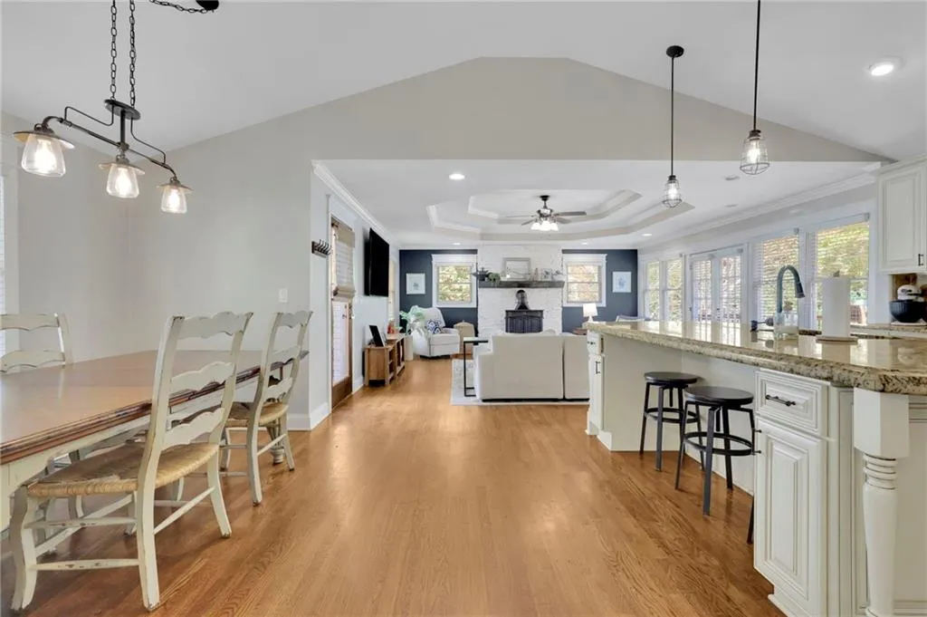 Kitchen with hanging light fixtures, ceiling fan, light hardwood / wood-style floors, light stone counters, and white cabinetry